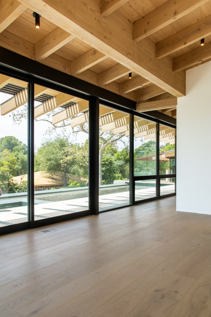 Room with full-height black-frame glass wall overlooking pool and tree canopy — La Cañada