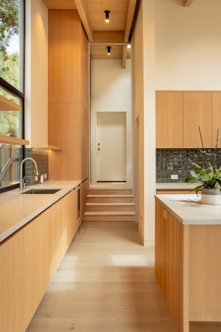Modern kitchen corridor with warm maple cabinetry and dark tile backsplash — La Cañada
